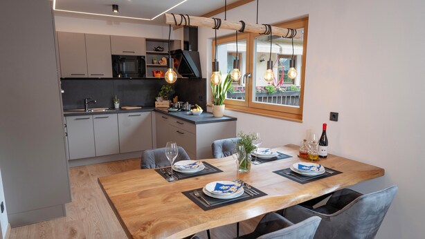 A modern kitchen with grey cabinets, a wooden dining table, and a view of a balcony with plants. - Modern apartment with mountain view (Chiusa)