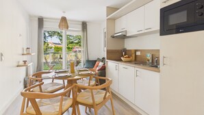 Una cucina moderna con mobili bianchi, un forno a microonde nero e una zona pranzo con sedie di legno e un tavolo rotondo.
