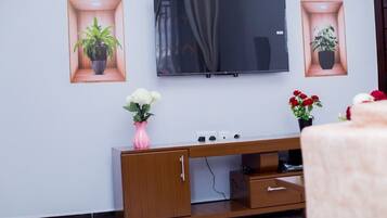 Una sala de estar con un televisor de pantalla plana montado en la pared, un mueble de madera debajo y dos macetas enmarcadas a cada lado del televisor.