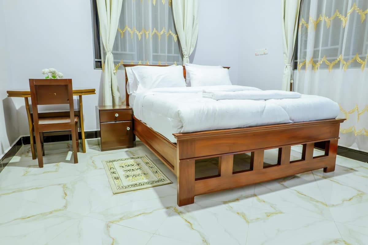 Un dormitorio con una cama de madera, una silla de madera, una mesita de noche y una mesita auxiliar.