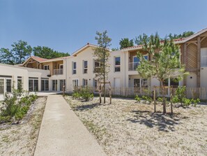 Um edifício moderno com várias varandas, um caminho pavimentado e vegetação escassa.