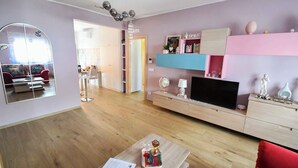 Una sala de estar moderna con piso de madera, un televisor sobre un mueble de madera, un sofá rojo, una mesa de centro con un libro y un espejo en la pared.