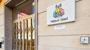 Entrada de un edificio con puerta de vidrio, un letrero que dice 'B&B Maison Glénis' y una placa debajo.