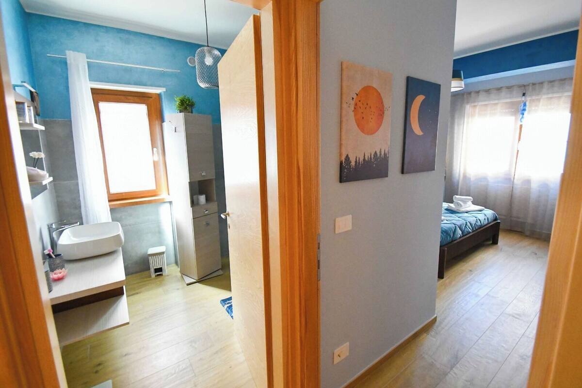 A bedroom with a bed, a nightstand, a window with curtains, and a wall with two paintings.