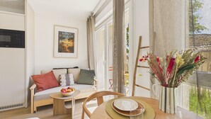 Un salon chaleureux avec un canapé, une table à manger où sont disposés des croissants, un saladier rempli de fruits et un vase de fleurs.