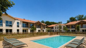 Un espace aménagé au bord de la piscine, comprenant une piscine rectangulaire, une terrasse en bois et des chaises longues.