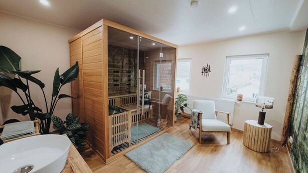 A room with a wooden cabinet, a white chair, a round side table, and a large plant. - High-quality vacation apartment with sauna and fitness (Tholey)