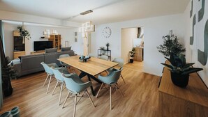 A modern living room with a wooden dining table, grey sofa, and a TV. - High-quality vacation apartment with sauna and fitness (Tholey)