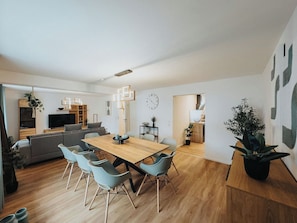 A modern living room with a wooden dining table, grey sofa, and a TV. - High-quality vacation apartment with sauna and fitness (Tholey)