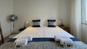 A hotel room with a bed, two bedside lamps, a standing fan, and a window with curtains. - Lagos Design 5 by Homing (Lagos)