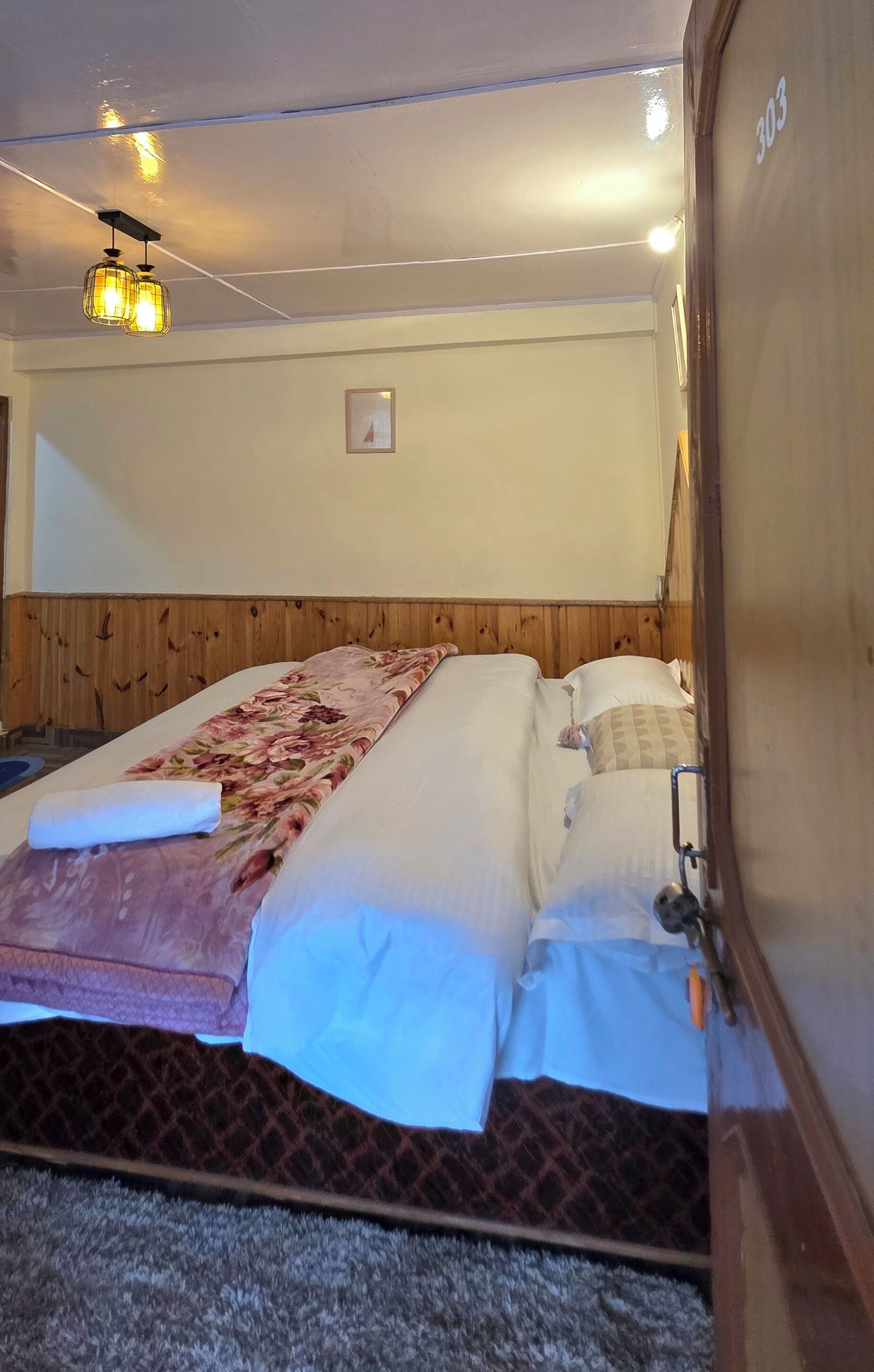 A room with a bed, wooden headboard, a hanging light fixture, and a door with a number.
