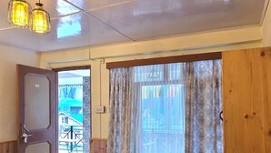 Una habitación con cama, una mesa con flores, un tapete estampado y vistas a través de cortinas.