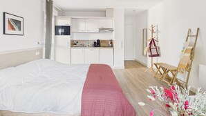 Un dormitorio con cama, una manta roja, kitchenette y una silla de madera.