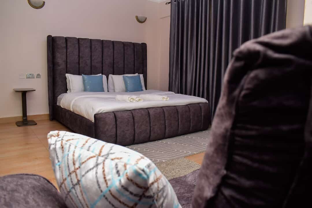 Un dormitorio con una cama grande, una mesita de noche, una silla y una ventana con cortinas.