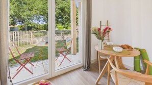 Ein Zimmer mit Esstisch, Stühlen, einer Obstschale, einer Blumenvase und Blick auf einen Garten durch große Fenster.