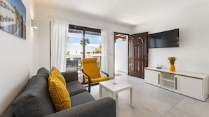 Una sala de estar moderna con un sofá, una mesa de centro, un sillón amarillo, un televisor montado en la pared y un ventanal corredizo que da a un espacio exterior.