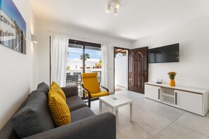 Ein modernes Wohnzimmer mit einer Couch, einem Couchtisch, einem gelben Sessel, einem an der Wand befestigten Fernseher und einer Schiebetür zu einem Außenbereich.