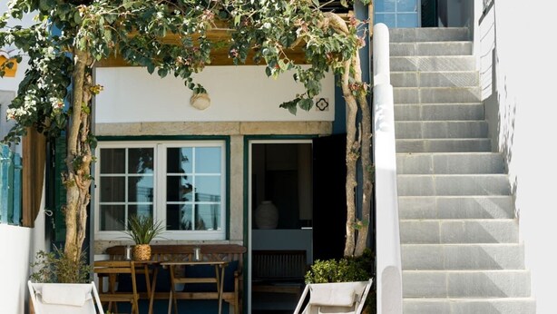 Una escalera que lleva a la entrada de un edificio, una mesa de madera con sillas y una planta en maceta.