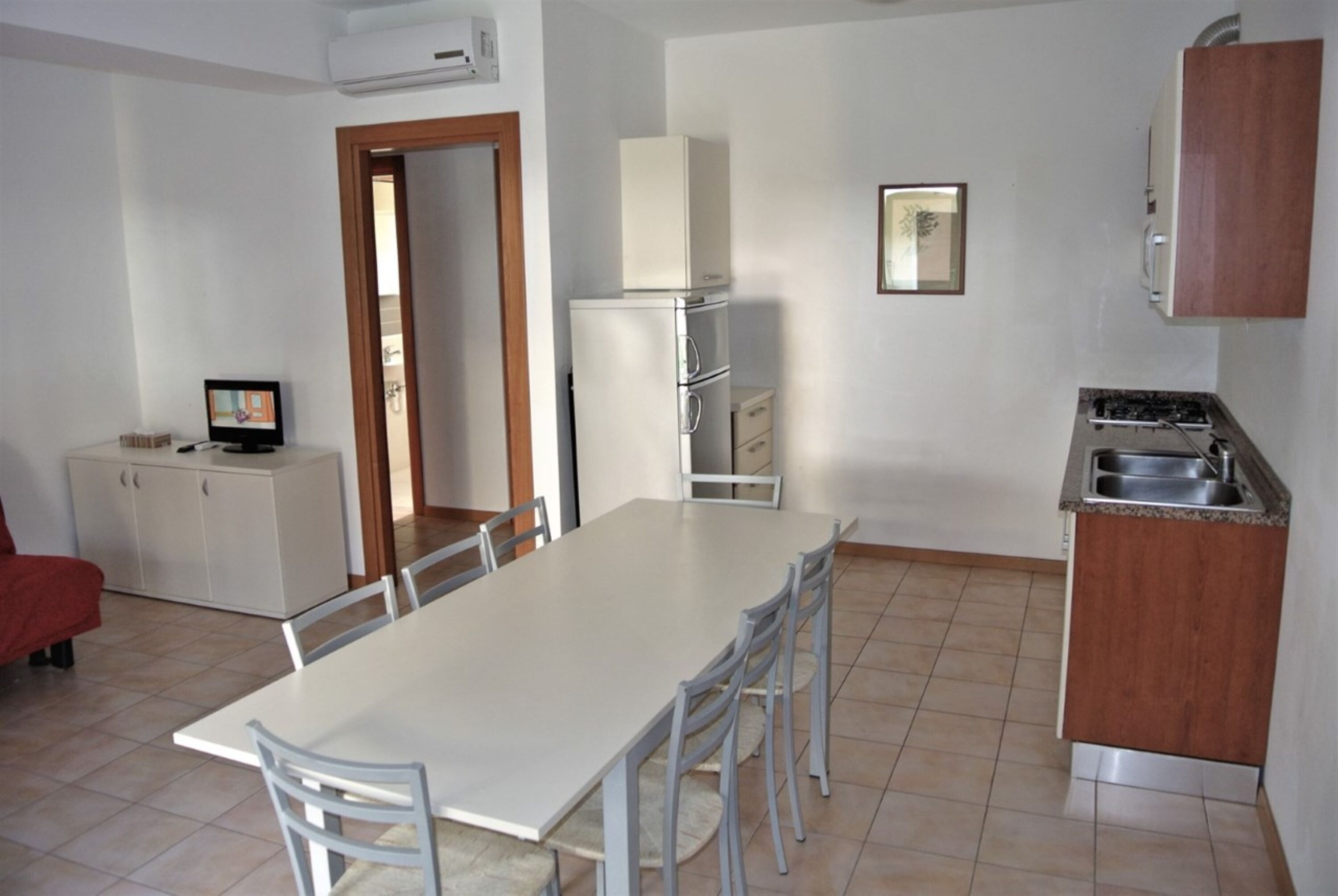 A compact kitchen with a dining table, chairs, a refrigerator, a stove, and a small cabinet.