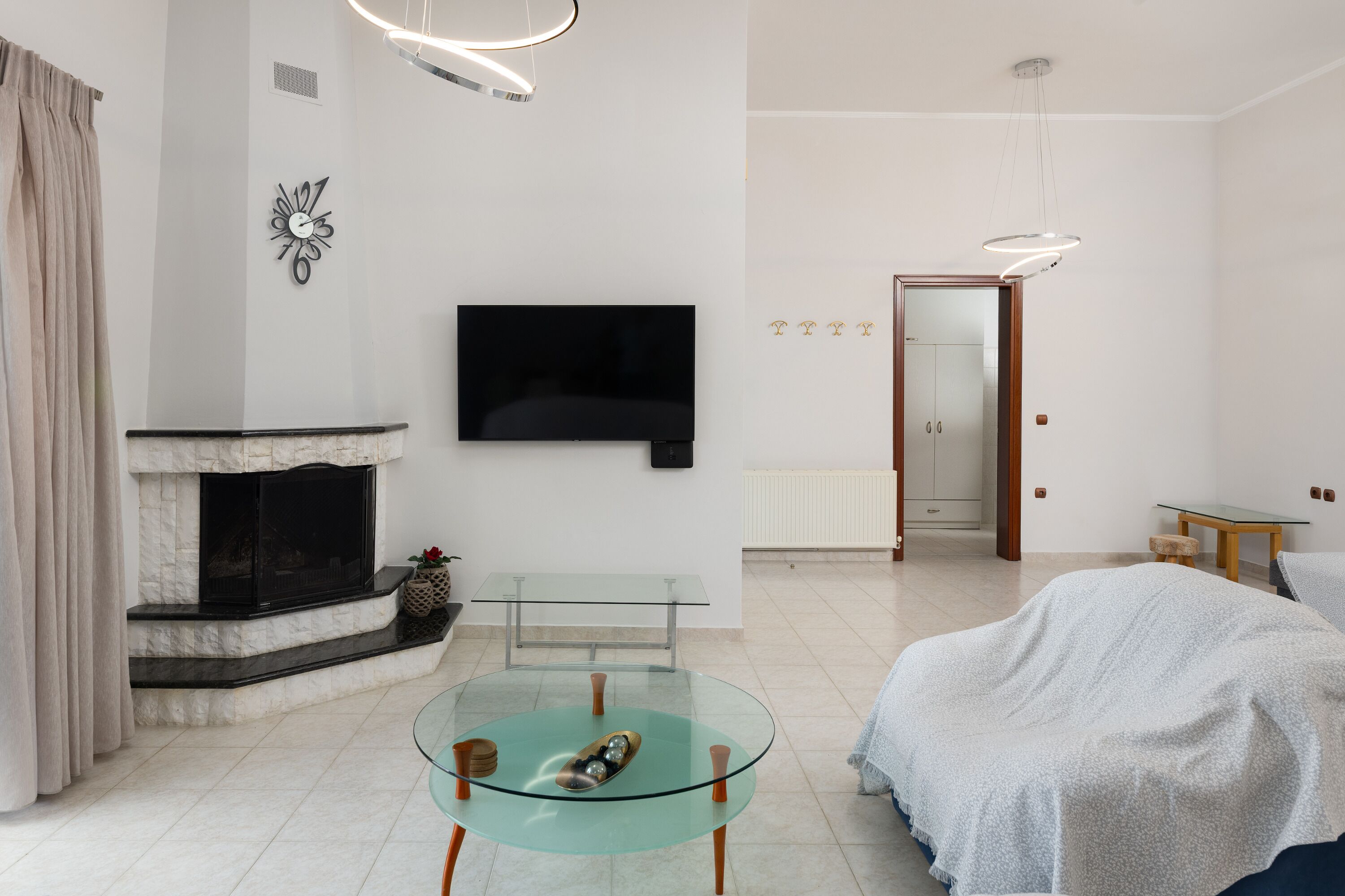 A modern living room with a fireplace, a flat-screen TV, a glass coffee table, and a bed with a blanket.