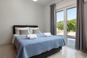 Ein Schlafzimmer mit einem Bett, Kissen, einer blauen Steude und Blick auf einen Garten durch eine Schiebetür.