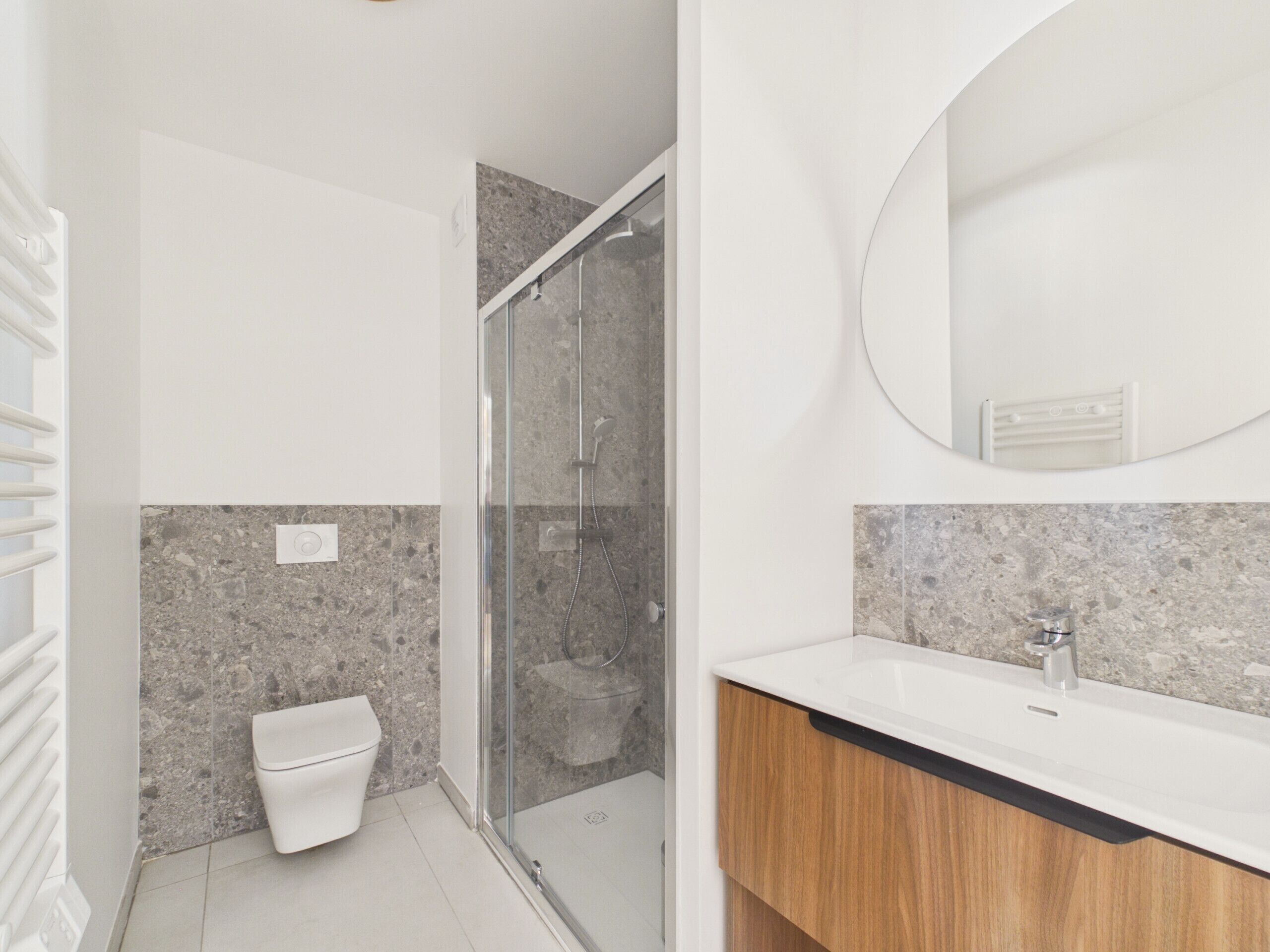Un baño moderno con ducha de mampara de vidrio, inodoro blanco y lavamanos sobre encimera de granito.