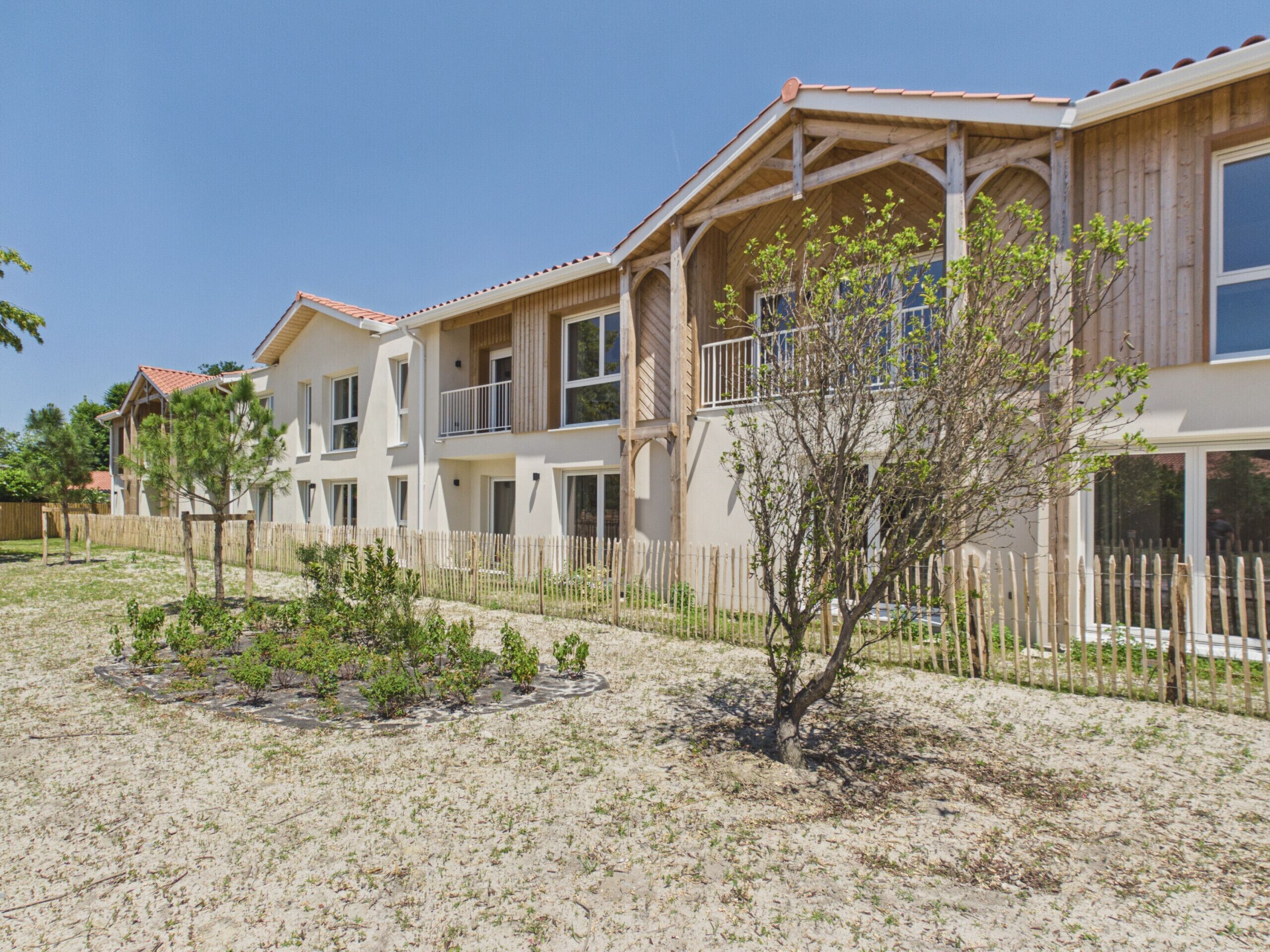 A multi-story residential building with a wooden facade, multiple balconies, and a fenced yard with sparse vegetation.