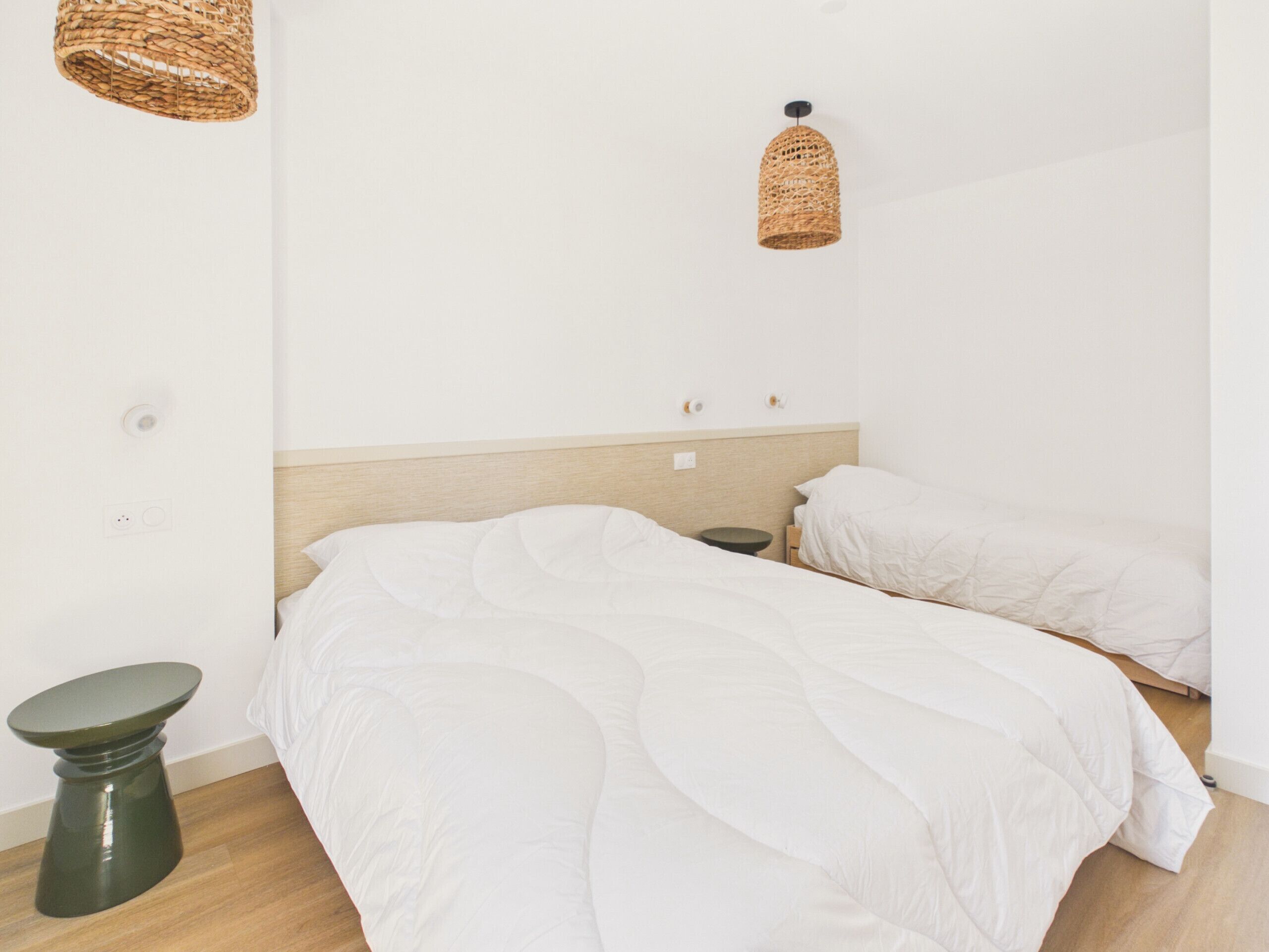 A bedroom with two beds, a bedside table, a floor lamp, and a wall-mounted light fixture.