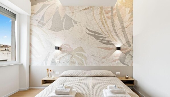 Un dormitorio moderno con una cama grande, vistas por una ventana y una pared con diseño de hojas.