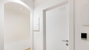 A hallway with a white door labeled '101' and a wall-mounted device. - Essentia Boutique Rooms 101 – Essential comfort in the heart of Cagliari ✨ (Cagliari)