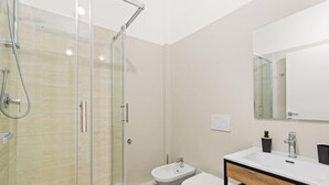 A modern bathroom with a glass shower enclosure, a sink, and a mirror. - Essentia Boutique Rooms 101 – Essential comfort in the heart of Cagliari ✨ (Cagliari)