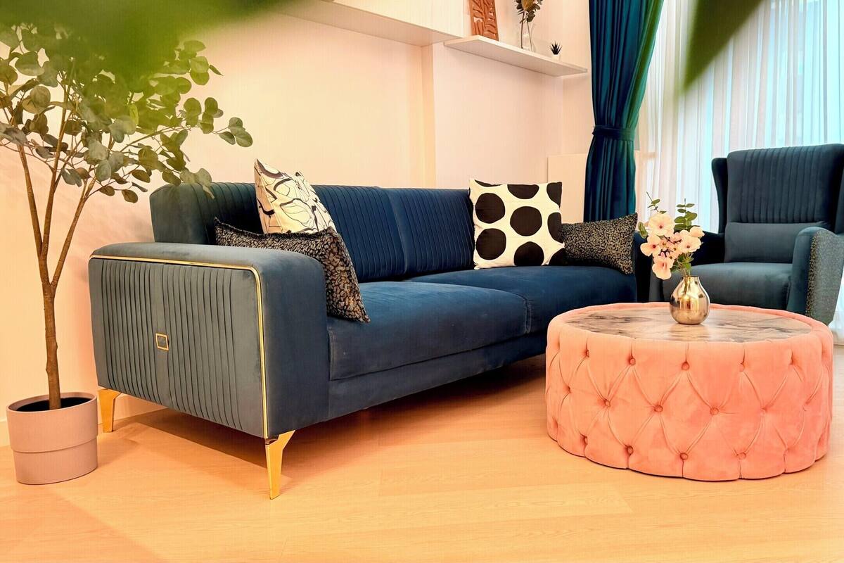 Una sala moderna con un sofá, un reposapiés y un sillón, una planta en maceta y un jarrón con flores.