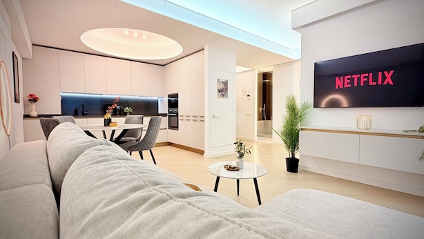 Una sala de estar moderna con un sofá, un comedor, una cocina y un televisor que muestra el logotipo de Netflix.