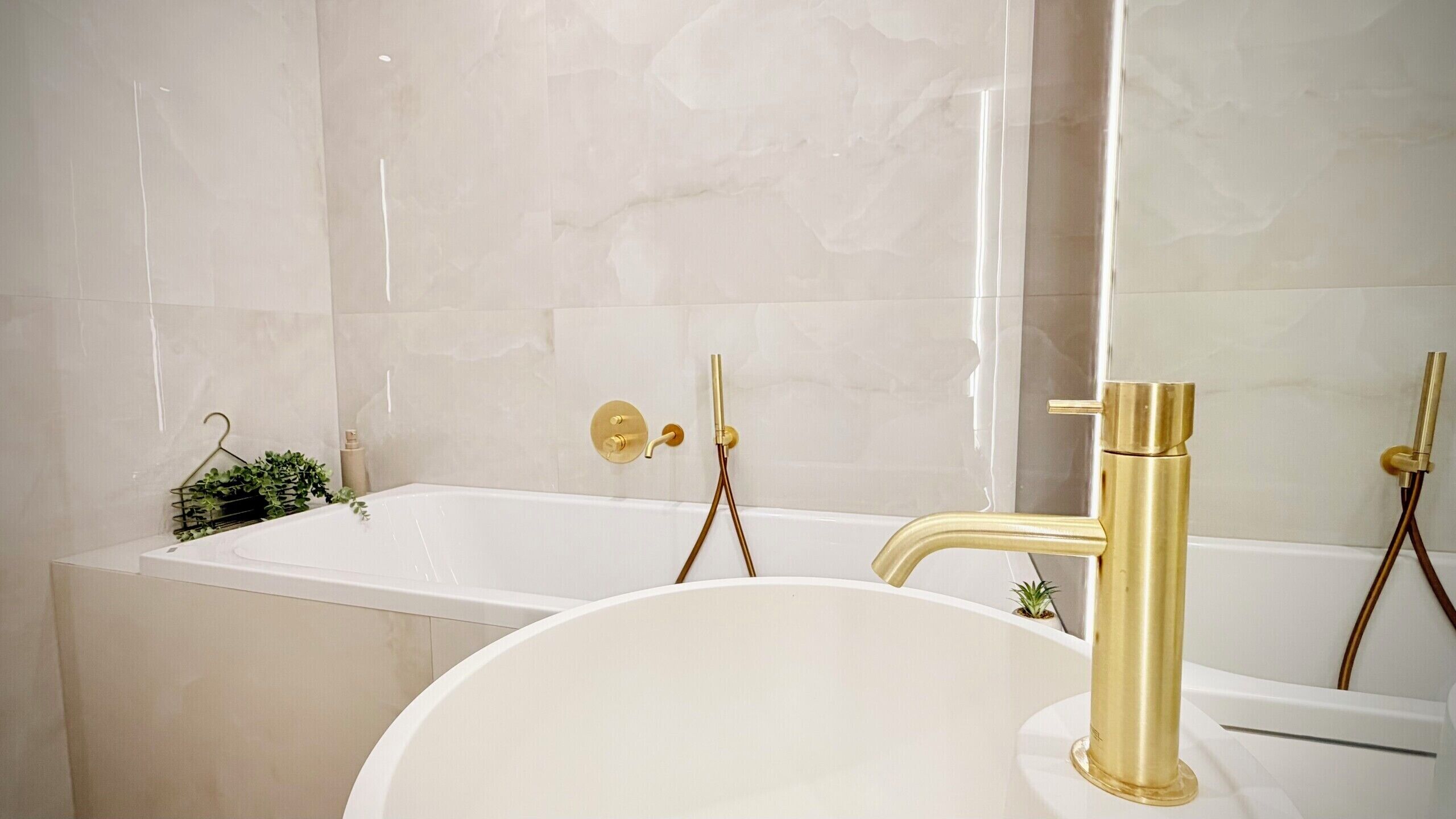 Ein Badezimmer mit einer weißen Badewanne, einem goldenen Wasserhahn und einem weißen Waschbecken.