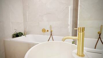 Ein Badezimmer mit einer weißen Badewanne, einem goldenen Wasserhahn und einem weißen Waschbecken.