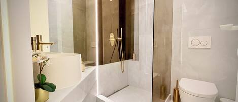 A modern bathroom with a glass-enclosed shower, a white sink, and a toilet.