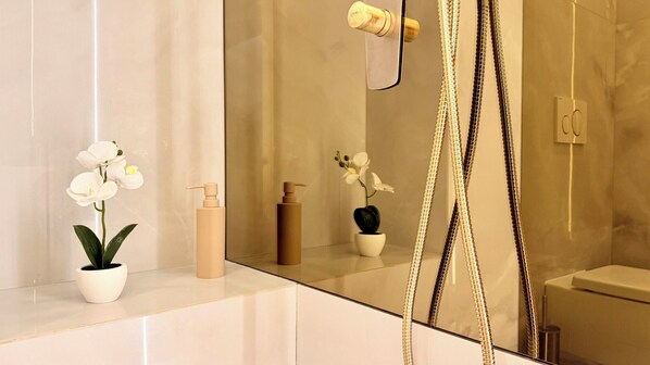 Un baño con cabina de ducha de vidrio, una orquídea en maceta y una botella de loción.