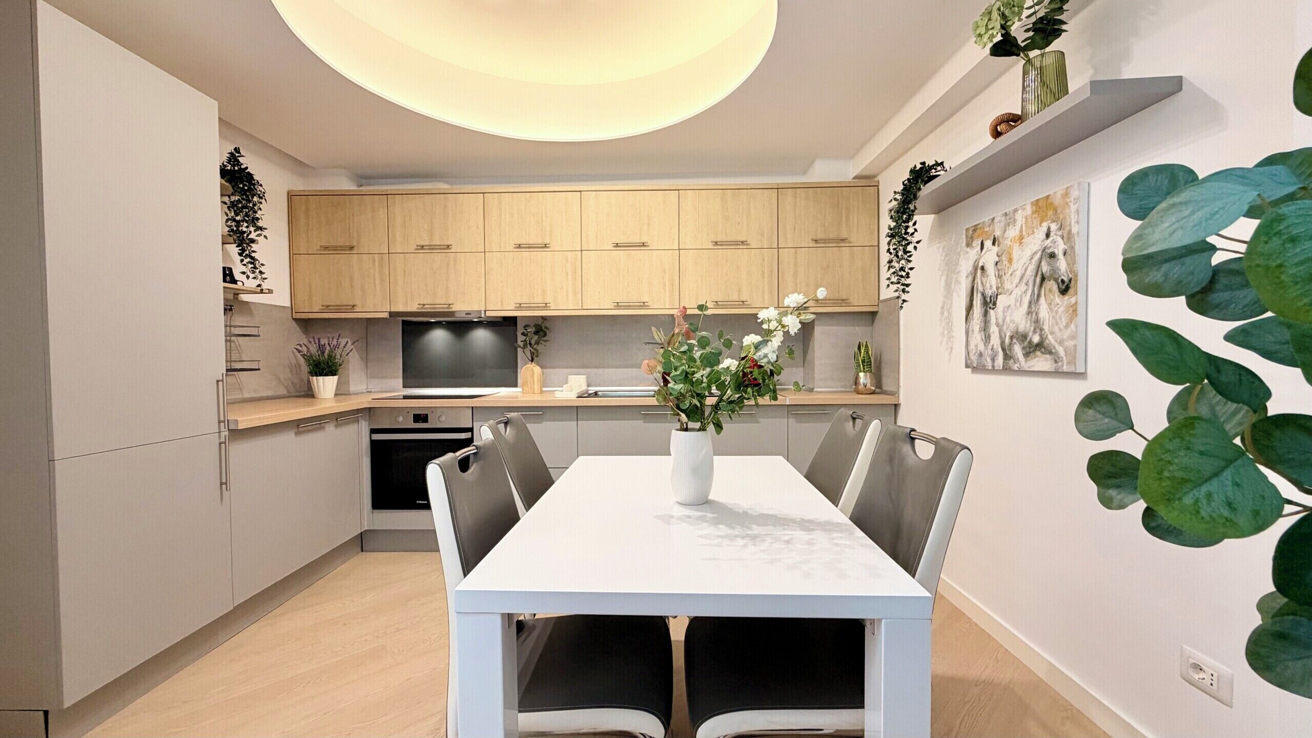 A modern kitchen with wooden cabinets, a dining table with chairs, and a vase with flowers.