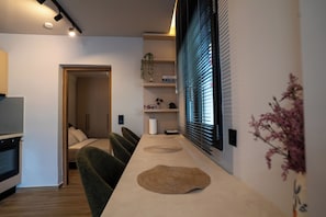 Eine moderne Küche mit Einbauofen, eine Essecke mit langem Tisch und Blick durch ein Fenster mit Jalousien.