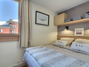 Un dormitorio con una cama, una ventana con cortinas, un cuadro enmarcado en la pared y un estante con cajas de almacenamiento.
