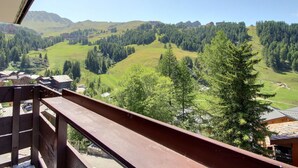 A balcony with a view of a mountainous landscape, including green fields and forested areas. - Beautiful 2-room apartment for 4 people, balcony, Plagne 1800 (La Plagne 1800)