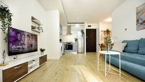 A modern living room with a flat-screen TV, wooden flooring, a blue sofa, and a kitchen in the background. - Urban Heaven in Aviatiei Business Area (Bucharest)