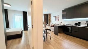 Quarto de hotel moderno com cama, área de refeições com mesa e cadeiras, cozinha com fogão e sala de estar com sofá.