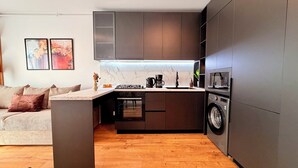 A modern kitchen with dark cabinetry, a built-in oven, a microwave, and a washing machine. - Urban Heaven in Aviatiei Business Area (Bucharest)