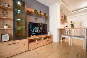 Uma sala de estar moderna com televisão de tela plana, estantes de madeira e um espaço de jantar com cadeiras brancas.