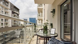 A balcony with a glass railing, a wicker chair, a small table with a vase, and a framed picture. - Urban Heaven in Aviatiei Business Area (Bucharest)