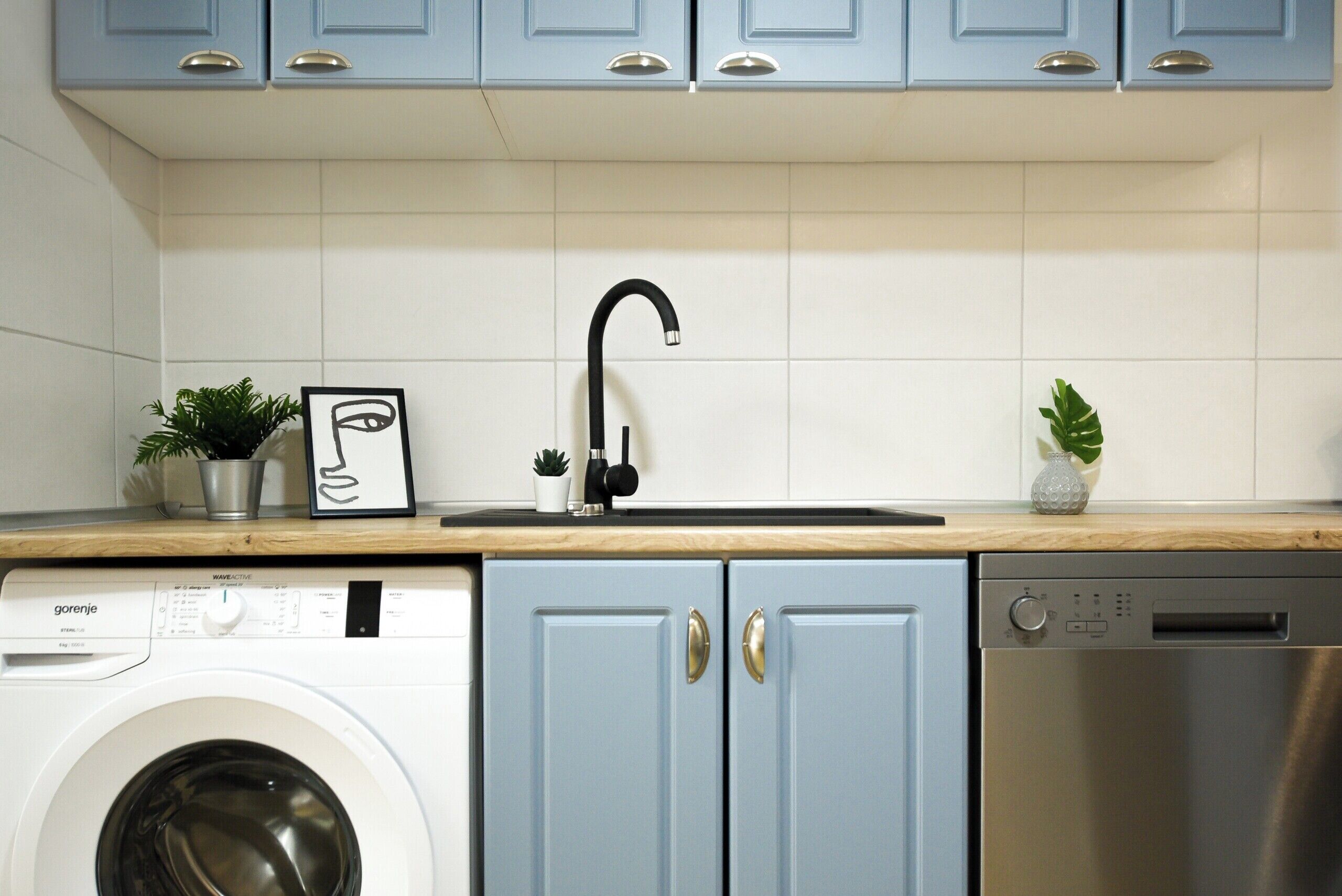 Een keuken met een wasmachine, vaatwasser en blauwe kastjes.