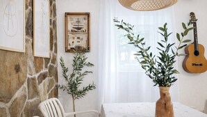 Ein Zimmer mit Steinsandsteinwand, einem weißen Stuhl, einem Tisch mit Pflanzenvasen, einer Gitarre und gerahmten Kunstwerken.