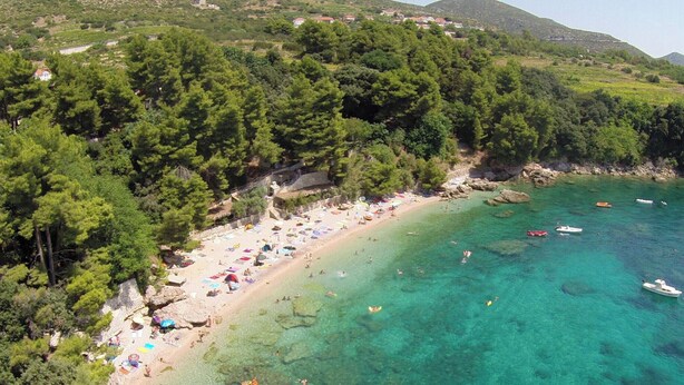 Eine Vogelperspektive zeigt einen Strand mit klarem türkisfarbenem Wasser, umgeben von dichtem Grünland und einigen in der Nähe verankerten Booten.