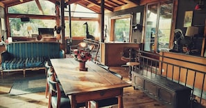 Una mesa de comedor de madera con sillas, un sofá azul y un ventanal con vista a árboles.